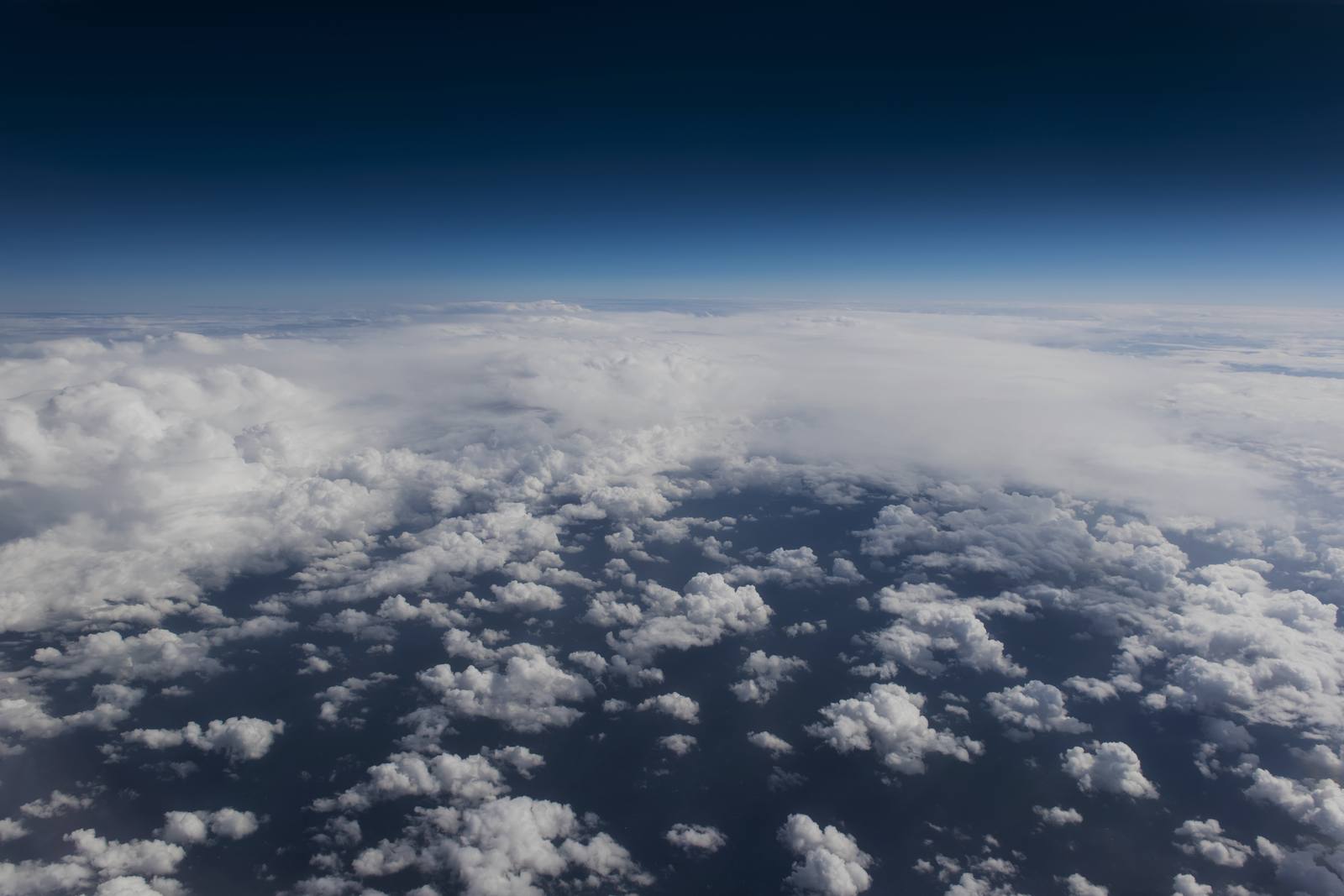 View from an aircraft window above a broken cloud deck under a deep blue sky